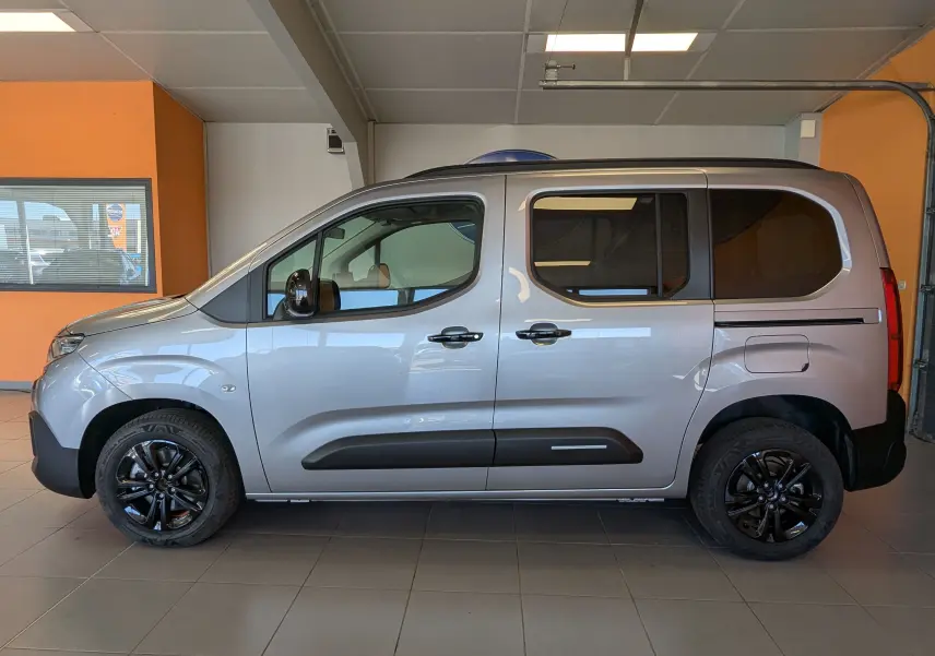 Profil droit du Citroën Berlingo gris Artense 2026 avec jantes noires et vitres teintées, en intérieur showroom.