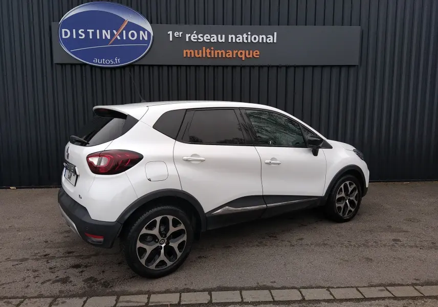 Renault Captur blanc vue de profil droit, avec jantes alliage et vitres arrière teintées, stationné devant un mur noir.