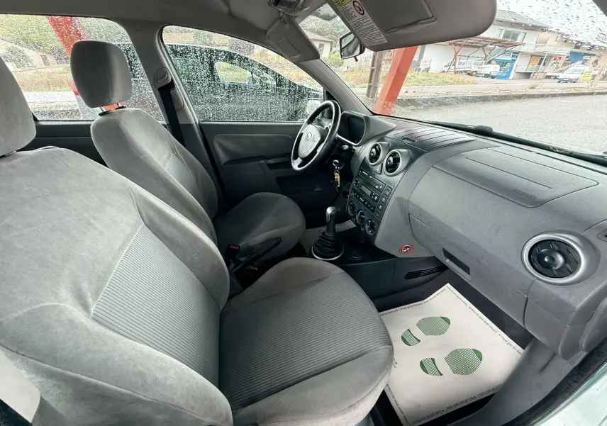 Intérieur avant droit d'une Ford Fusion 2002, sièges gris en tissu et tableau de bord simple sous la pluie.