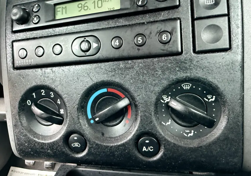 Gros plan sur la console centrale d'une Ford Fusion 2002, montrant les commandes de climatisation et la radio FM.