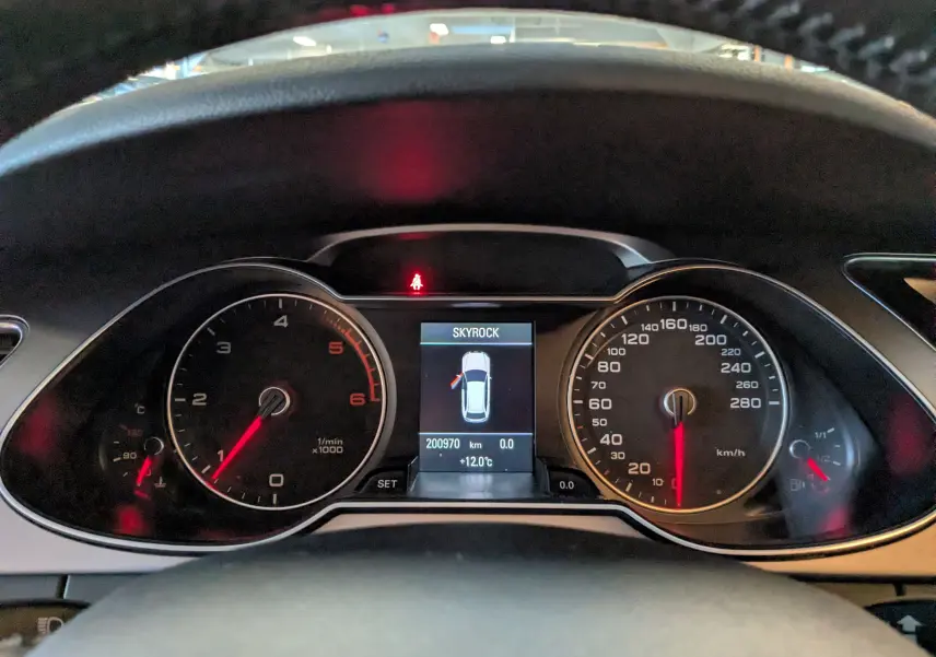 Tableau de bord de l'Audi A4 gris 2013 montrant compte-tours, vitesse et écran central avec porte ouverte à gauche.