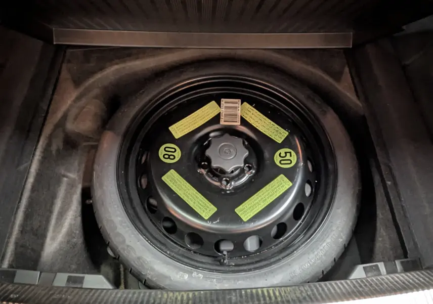 Vue en plongée sur la roue de secours noire avec étiquettes jaunes dans le coffre d'une Audi A4 gris diesel 2013