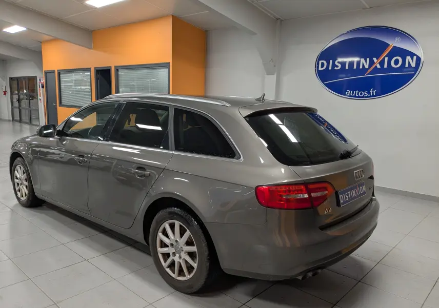 Audi A4 break gris vue 3/4 arrière droit en intérieur avec logo Distinxion en arrière-plan.