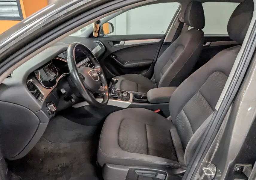 Vue intérieure côté conducteur de l'Audi A4 gris 2013, montrant les sièges noirs et le tableau de bord avec boîte manuelle.