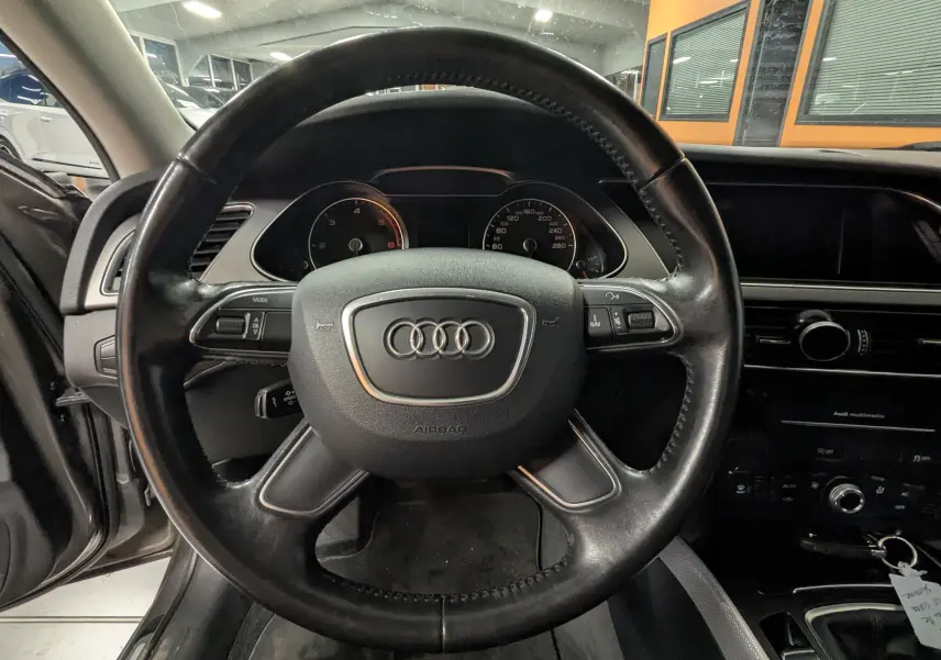 Vue rapprochée du volant en cuir noir de l'Audi A4 2013 avec tableau de bord et commandes visibles en arrière-plan