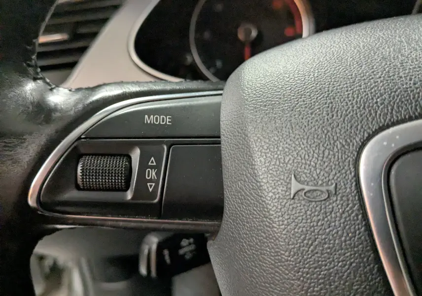 Gros plan sur la partie gauche du volant de l'Audi A4 gris 2013, montrant les commandes mode et OK.