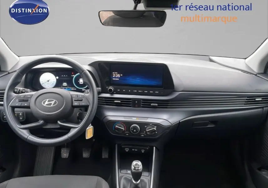Vue intérieure avant du tableau de bord gris d'une Hyundai i20 2025 avec volant cuir multifonction et écran tactile central.
