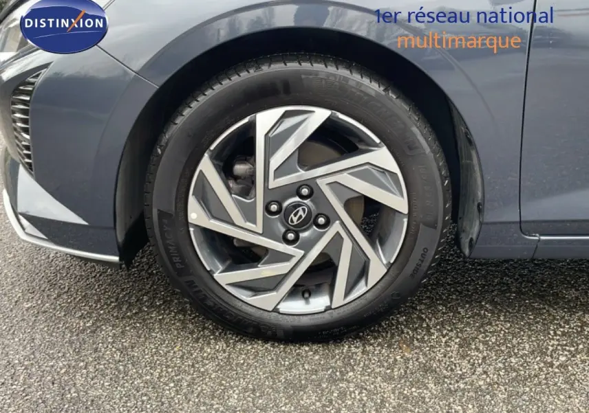 Gros plan sur la roue avant gauche d'une Hyundai i20 gris Aurora Metal avec jante alliage au design géométrique.