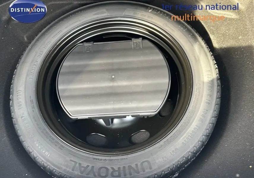 Pneu de secours noir monté dans le coffre d'une Citroën C5 Aircross blanc nacré, vue plongeante rapprochée.