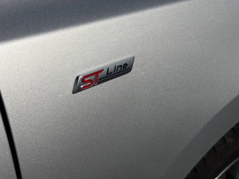 Gros plan sur l'écusson ST Line rouge et noir sur la carrosserie gris lunaire métallisé d'une Ford Focus SW 2023.
