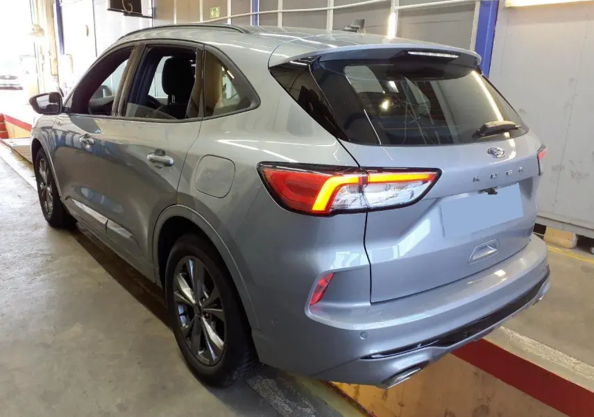 Vue 3/4 arrière droite du Ford Kuga gris Solar 2024 avec feux LED allumés et double sortie d'échappement ST-Line.