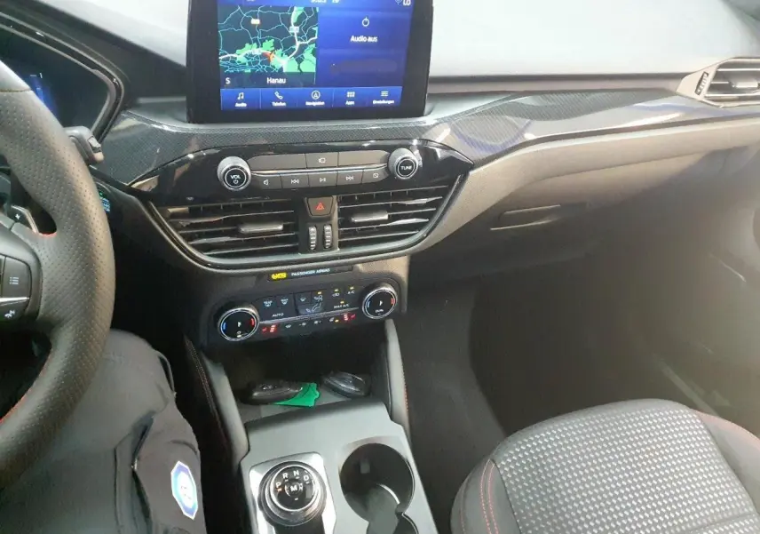 Vue intérieure du Ford Kuga 2024, tableau de bord et console centrale avec écran tactile et sélecteur rotatif gris.