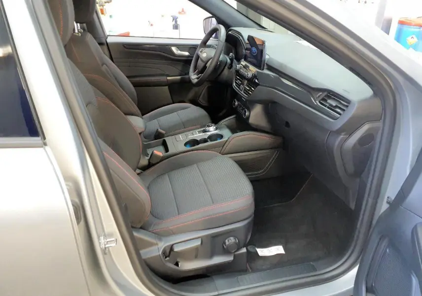 Vue intérieure côté conducteur du Ford Kuga gris Solar 2024, sièges noirs avec surpiqûres rouges et console centrale moderne.