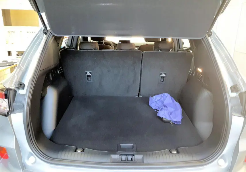 Coffre ouvert vu de l'arrière d'un Ford Kuga gris Solar 2024, avec intérieur noir et un tissu violet posé.
