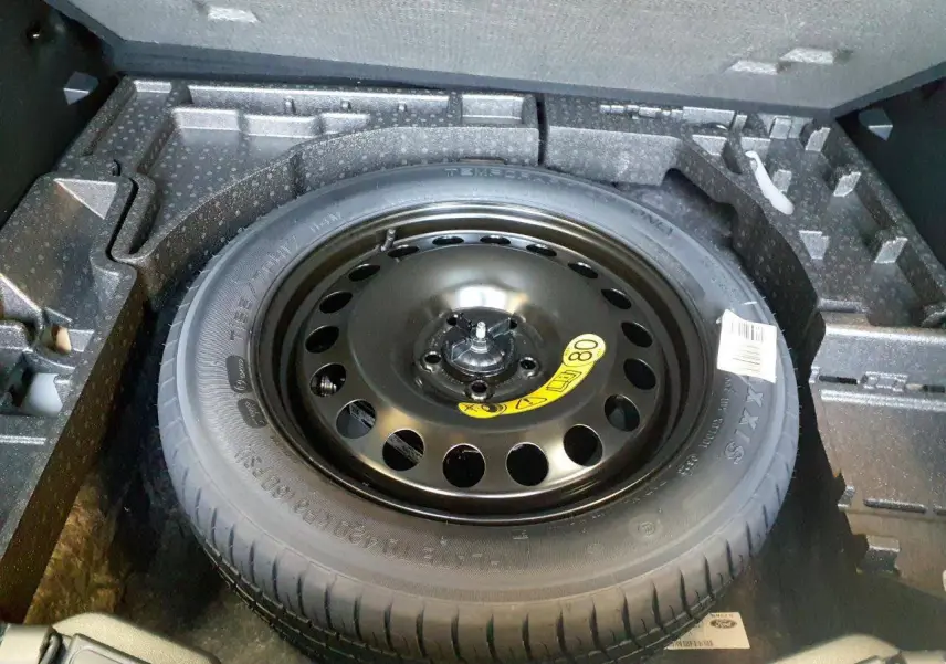 Roue de secours galette noire dans le coffre du Ford Kuga 2024, vue plongeante sur le pneu et son logement en mousse.