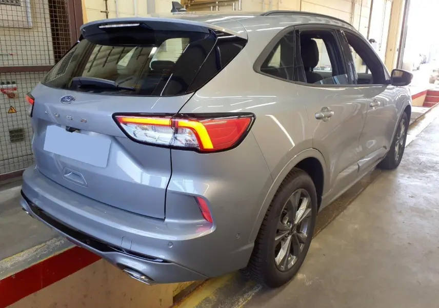 Vue 3/4 arrière droite du Ford Kuga gris Solar 2024 avec feux allumés et double sortie d’échappement ST-Line.