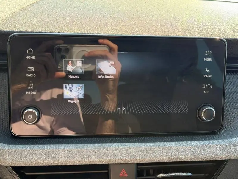 Écran tactile central noir du Skoda Scala 2025 avec commandes multimédia et boutons rotatifs sur tableau de bord gris.