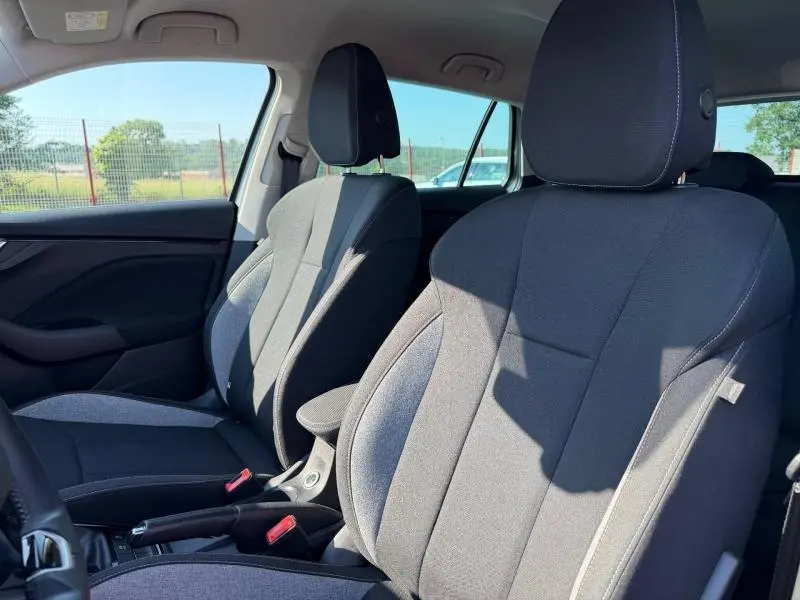 Vue intérieure des sièges avant en tissu noir et gris d'une Skoda Scala 2025, avec accoudoir central et ceintures rouges.