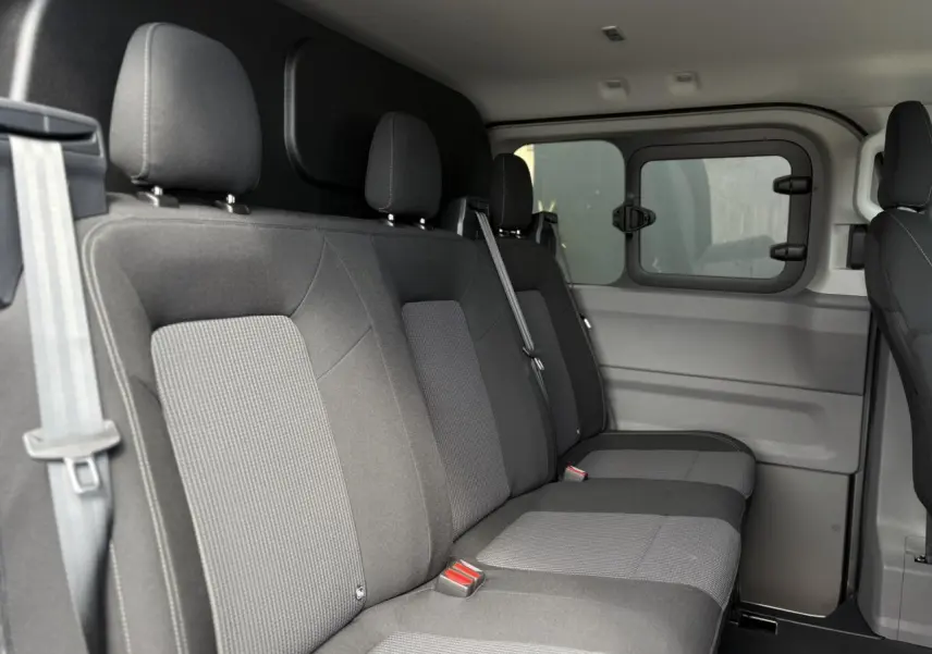 Vue intérieure côté droit des sièges arrière en tissu gris du Volkswagen Transporter T7 ProCab 2026, avec fenêtre coulissante.