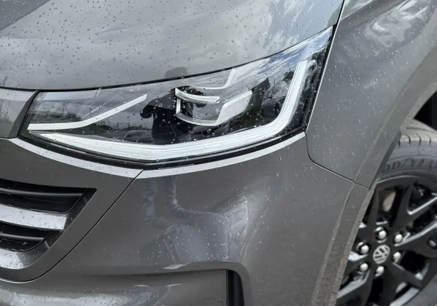 Gros plan sur le phare avant droit LED et la jante alliage noir brillant du Volkswagen Transporter T7 gris graphite mouillé.