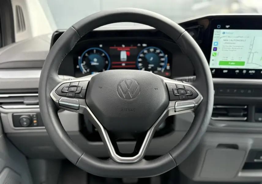 Vue rapprochée du volant multifonction en similicuir noir du Volkswagen Transporter T7 avec tableau de bord digital et écran tactile.
