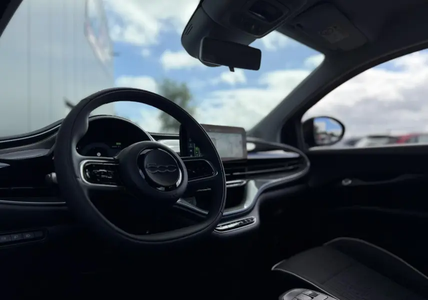 Vue intérieure côté conducteur de la Fiat 500 électrique 2024 en Noir Onyx, volant Soft-Touch et écran tactile central visible.