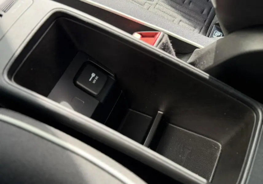 Gros plan sur le rangement central intérieur de la Fiat 500 électrique 2024, avec prise 12V visible et sellerie noire.