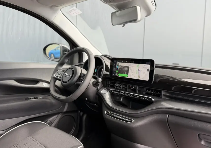 Intérieur de la Fiat 500 électrique 2024, vue côté conducteur, tableau de bord noir brillant avec écran tactile central.