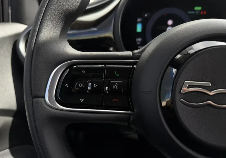 Gros plan sur le volant noir Soft-Touch du Fiat 500 électrique 2024 avec commandes intégrées et logo 500 au centre.