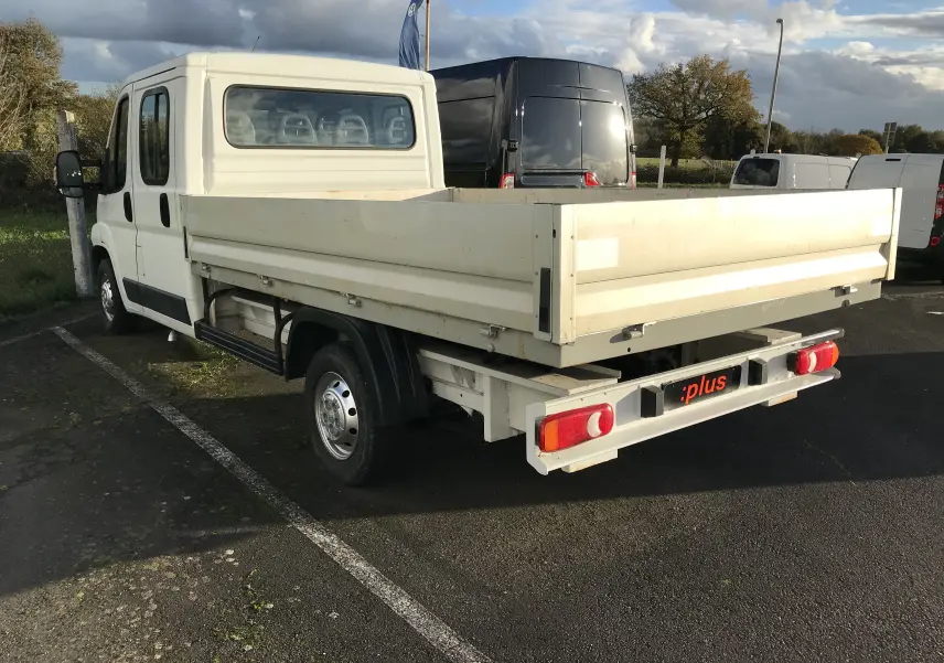 Vue 3/4 arrière gauche d'un Peugeot Boxer blanc plateau double cabine 7 places stationné en extérieur.