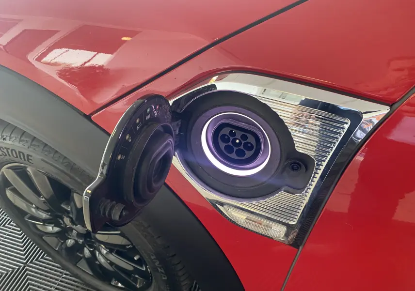 Prise de recharge ouverte côté gauche sur MINI Countryman Cooper SSE rouge toit noir, avec jante noire visible.