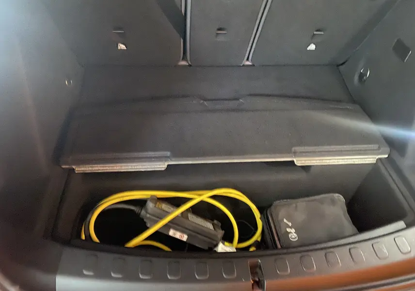 Coffre ouvert d'une MINI Countryman rouge toit noir, montrant le rangement avec câble de recharge hybride et trousse noire.
