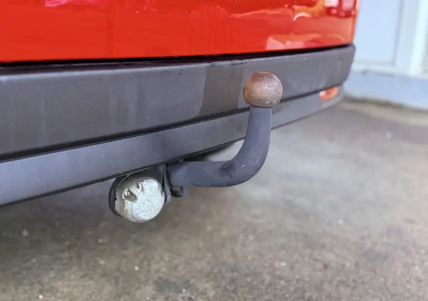 Gros plan sur l'attelage d'une FIAT Doblo Cargo rouge, avec pare-chocs arrière noir et prise électrique visible.