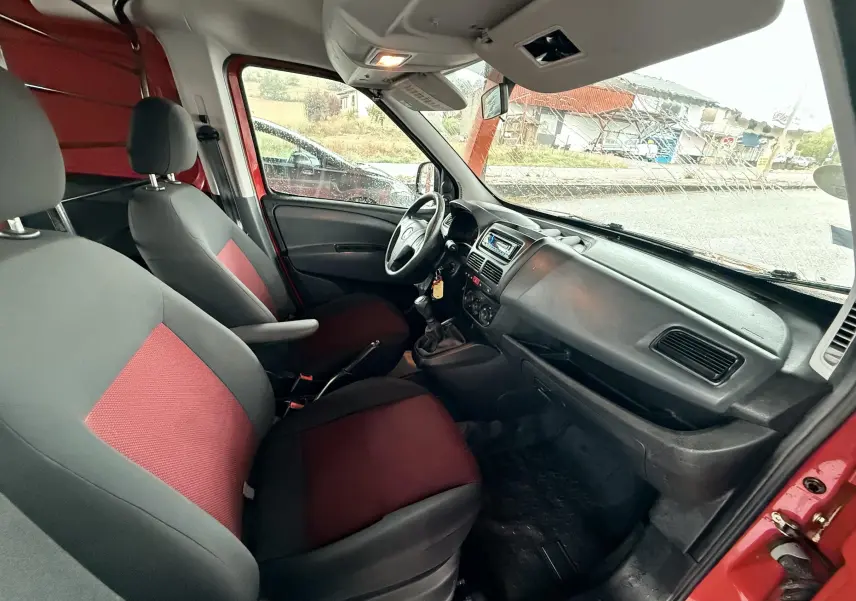 Vue intérieure côté conducteur du Fiat Doblo Cargo rouge de 2011, sièges tissu rouge et noir, tableau de bord simple.