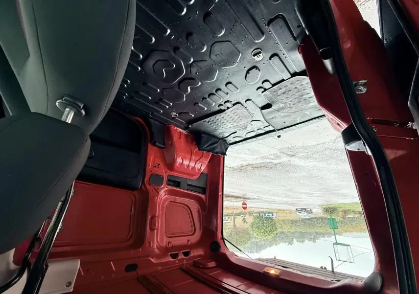 Vue intérieure arrière du FIAT Doblo Cargo rouge montrant l'espace de chargement vide et la porte ouverte côté droit.