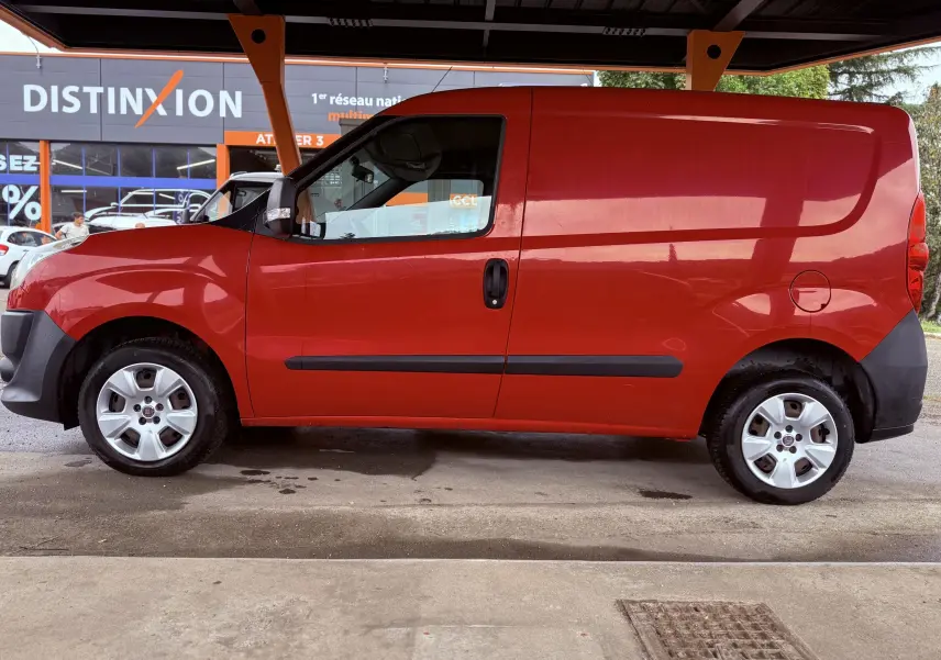 Vue de profil côté gauche d’un FIAT Doblo Cargo rouge de 2011, fourgon compact avec jantes argentées et poignées noires.