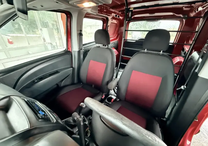 Vue intérieure avant du Fiat Doblo Cargo rouge de 2011, sièges tissu noir et rouge avec cloison métallique arrière.
