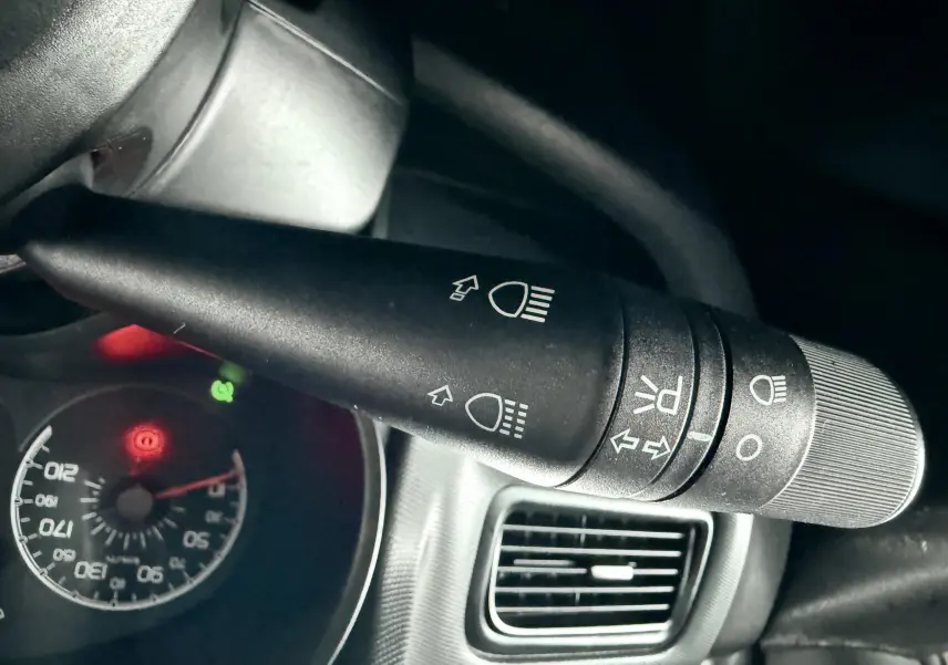 Gros plan sur la commande des phares et clignotants dans l’habitacle du Fiat Doblo Cargo rouge, tableau de bord partiellement visible.