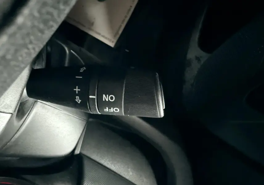 Gros plan sur la commande de régulateur de vitesse noire à gauche du volant dans l'habitacle du Fiat Doblo Cargo 2011.