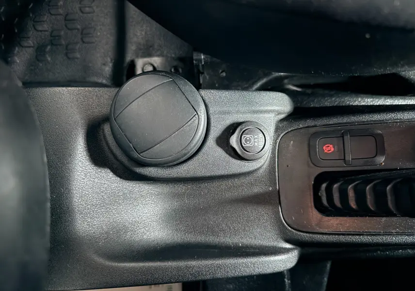 Gros plan sur la console centrale noire du Fiat Doblo Cargo 2011, montrant une prise 12V et un bouton de frein à main électrique.