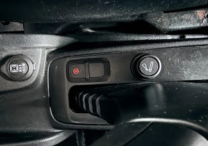 Gros plan sur la console centrale noire du Fiat Doblo Cargo 2011 montrant les boutons de commande et prise 12V.
