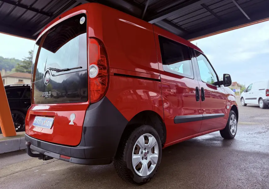 Fiat Doblo Cargo rouge vu en 3/4 arrière droit sous abri, avec hayon noir et protections latérales noires.