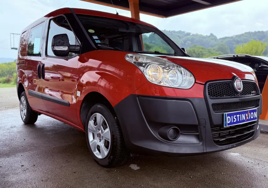 Fiat Doblo Cargo rouge vue 3/4 avant droit sous abri avec pare-chocs noir et plaques Distinxion.
