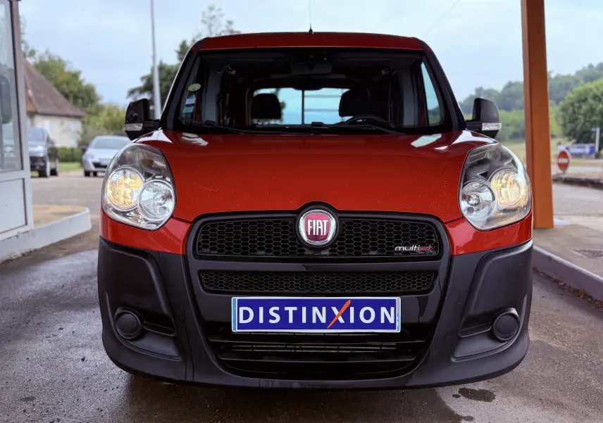 Vue frontale d'un FIAT Doblo Cargo rouge avec phares allumés et calandre noire, immatriculé Distinxion.