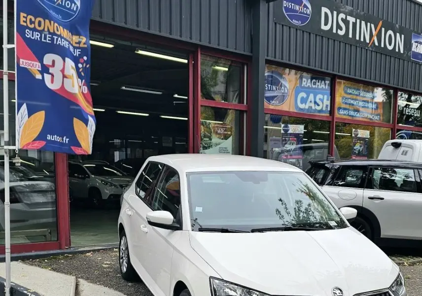 Vue 3/4 avant d'une Skoda Fabia blanche Cristal garée devant un garage avec calandre noire et feux LED.