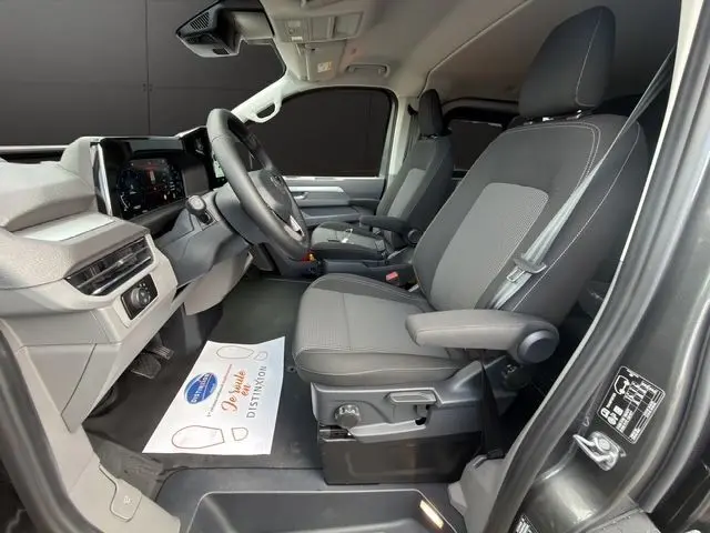 Vue intérieure côté conducteur du Volkswagen Transporter ProCab gris, montrant les sièges avant en tissu rayé et le tableau de bord moderne.