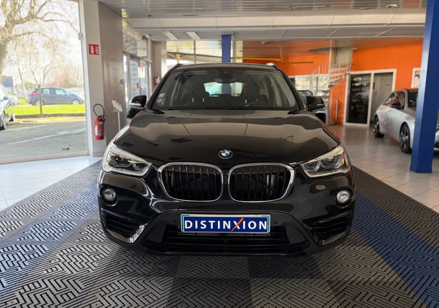 Vue avant d'un BMW X1 noir 2018 en showroom, mettant en valeur sa calandre double haricot et ses phares LED distinctifs.