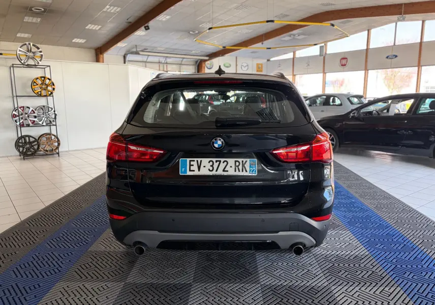 Vue arrière d’un BMW X1 noir 2018 dans un showroom, avec feux rouges et double sortie d’échappement visibles.