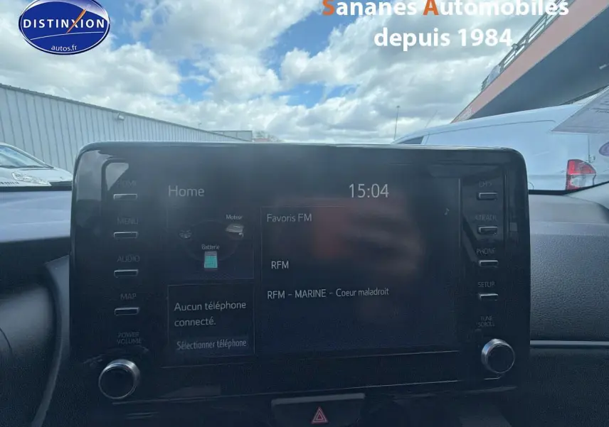 Écran tactile central de la Toyota Yaris Hybrid 2023, affichant la radio FM, avec tableau de bord en arrière-plan.