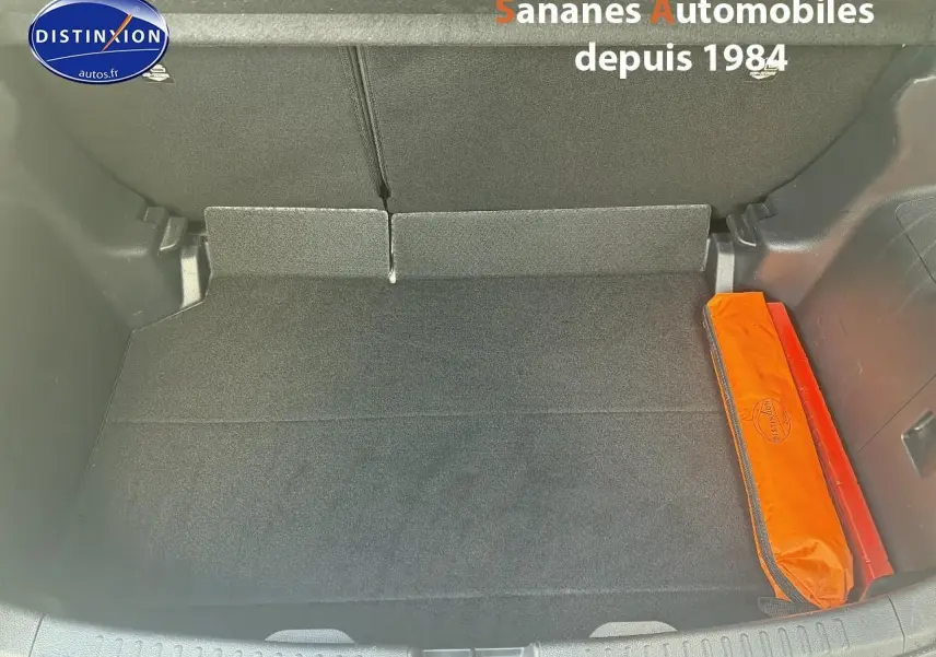 Coffre ouvert de Toyota Yaris Hybrid 116h 2023 en peinture INC, montrant un rangement avec trousse de secours orange.